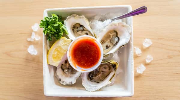 A plate of freshly shucked oysters is presented on the half shell, served with lemon wedges and a side of cocktail sauce for a bright, briny seafood experience.