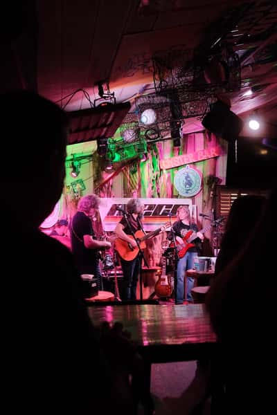 Live band performing on stage at Stinky's Bait Shack oyster bar, with colorful lights and guests watching from tables.