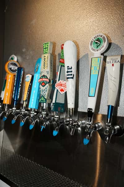 Row of bar draft beer taps featuring a variety of craft and domestic beers, including Miller Lite and Michelob Ultra, mounted on a stainless steel tap wall.