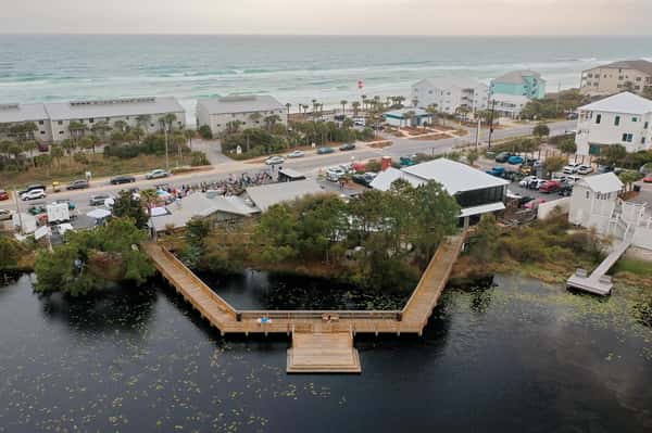 Aerial view of Stinky's Bait Shack near the beach with boardwalk over the coastal lake, nearby homes, and the Gulf of Mexico in the background.