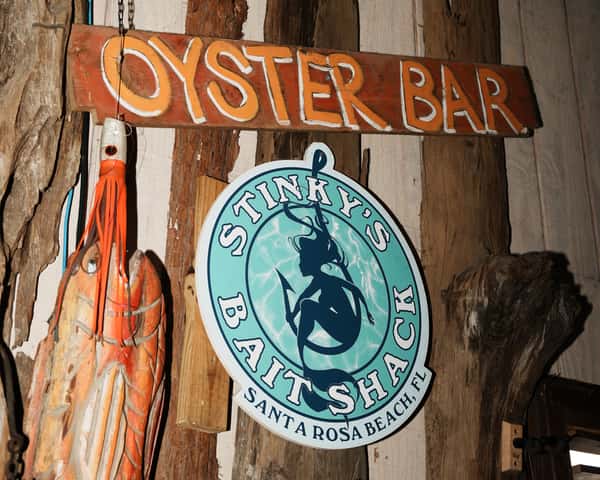 Rustic "Oyster Bar" sign and Stinky's Bait Shack logo mounted on driftwood-style wall décor inside a coastal seafood restaurant