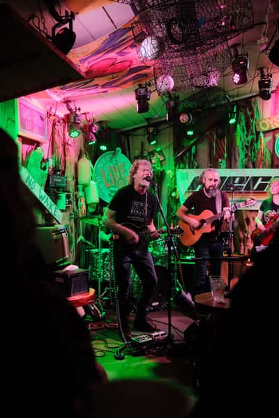 Live band performing on stage at Stinky's Bait Shack oyster bar, with colorful lights and guests watching from tables.