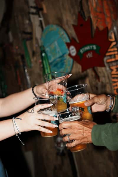 Friends clinking drinks—beer and cocktails—in branded cups at Stinky's Bait Shack, with rustic fishing-themed décor in the background. 🍻