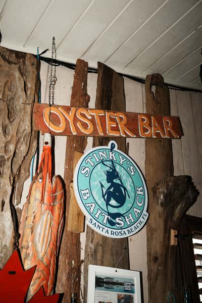 Rustic "Oyster Bar" sign and Stinky's Bait Shack logo mounted on driftwood-style wall décor inside a coastal seafood restaurant.