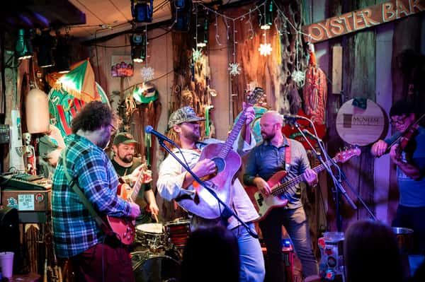 Live band performing on a colorful stage at Stinky's Bait Shack oyster bar with guitars, fiddle, and festive lighting.