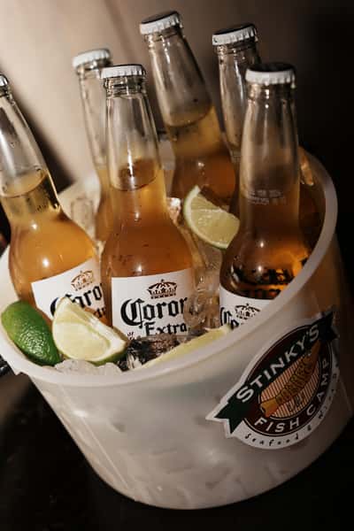 Bucket of Corona Extra beers on ice with lime wedges served in a branded Stinky's Fish Camp bucket.
