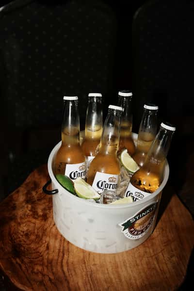 Bucket of Corona Extra beers on ice with lime wedges served in a branded Stinky's Fish Camp bucket.