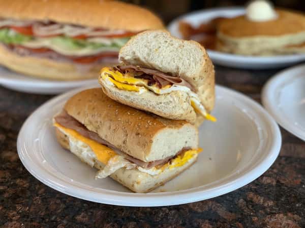 bacon, ham, egg, and cheese on a roll with sesame seeds