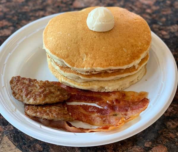 stack of pancakes with butter with a side of bacon and sausage on a plate