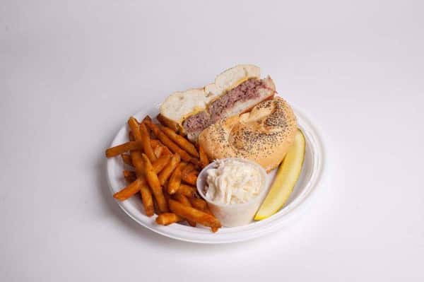 roastbeef and cheese sandwich on a plate with sweet potato fries, a pickle, and coleslaw
