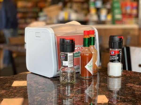 napkin holder with salt, pepper, and two bottles of hot sauce on a table