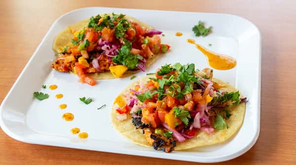 Three tacos with purple cabbage, mango salsa, and cilantro, served in a foil to-go container.