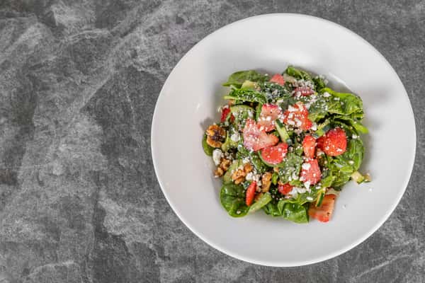 Overhead view of a fresh salad featuring mixed greens, diced tomatoes, colorful vegetables, and crumbled cheese, served in a white bowl.