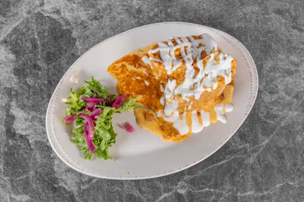 Golden breakfast dish topped with a generous drizzle of creamy white sauce and seasonings, served with a colorful side salad on a white plate.