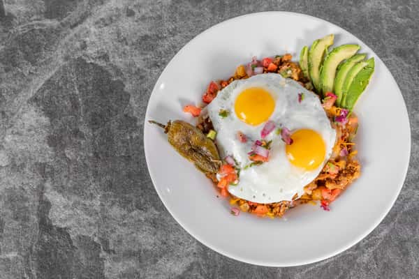 Breakfast plate featuring two sunny-side-up eggs served over a colorful mixture of vegetables and greens on toasted bread.