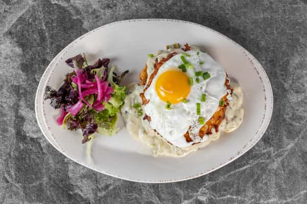 Overhead view of a brunch plate featuring a sunny-side-up egg on toast with creamy sauce and fresh herbs, served alongside a colorful purple cabbage slaw.