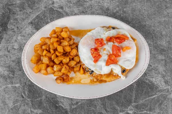 Breakfast plate featuring golden seasoned potatoes, two fried eggs, and diced tomatoes, served on a white plate.