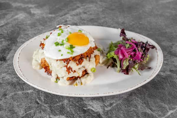 Breakfast toast topped with a sunny-side-up egg, creamy sauce, and fresh herbs, served on a white plate with a colorful purple cabbage slaw.