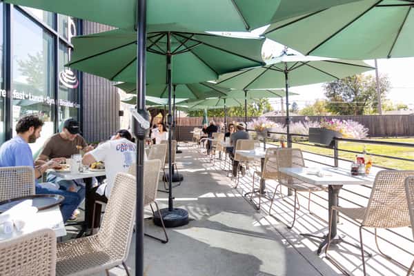 Outdoor restaurant patio with tables and chairs shaded by large green umbrellas, offering a welcoming space for guests to enjoy dining in the open air.