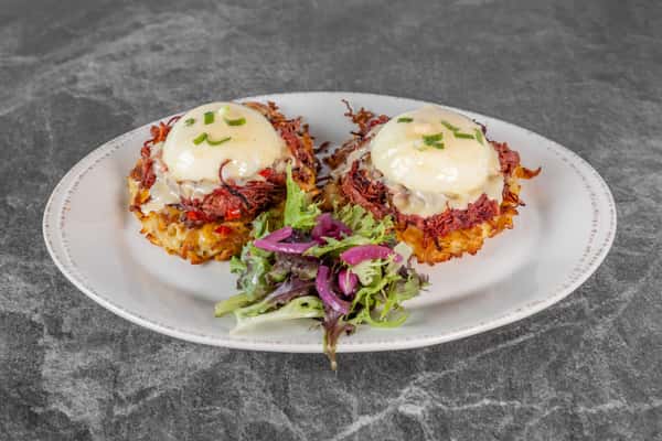 Two servings of eggs Benedict topped with poached eggs and creamy hollandaise sauce, served on a white plate with a colorful side salad.