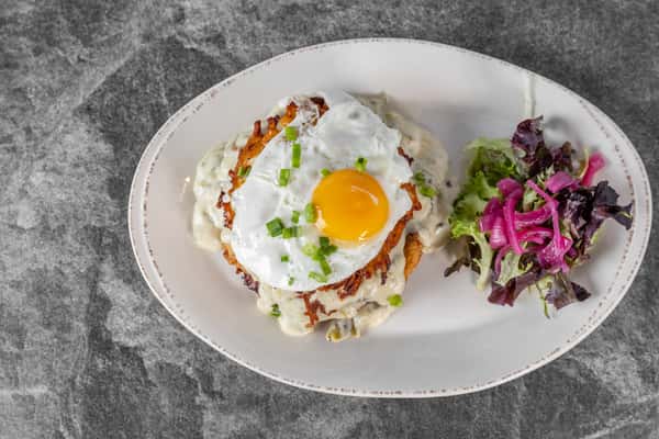 Overhead view of a sunny-side-up egg served on toast with creamy sauce and fresh herbs, accompanied by a colorful purple cabbage slaw.