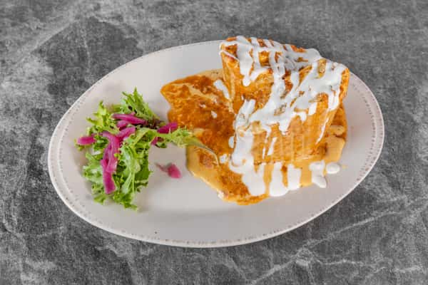 Golden, crispy breakfast dish topped with creamy white sauce and orange seasoning, served alongside a colorful side salad on a white plate.