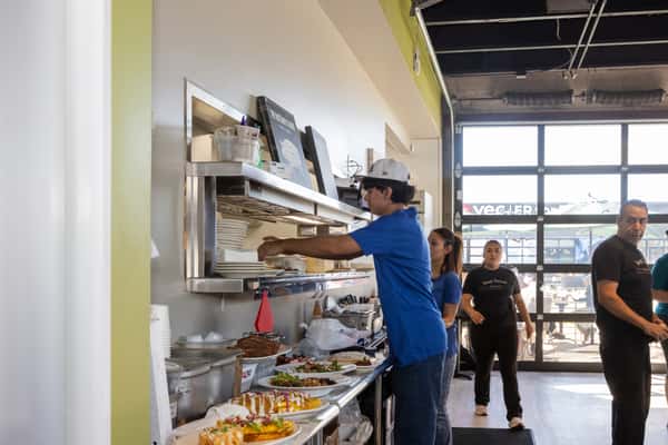Restaurant kitchen staff member wearing a blue shirt preparing food at a stainless steel counter in a bright, open kitchen.
