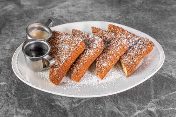 Golden French toast sticks dusted with powdered sugar, served on a white plate with two small cups of dipping sauce.