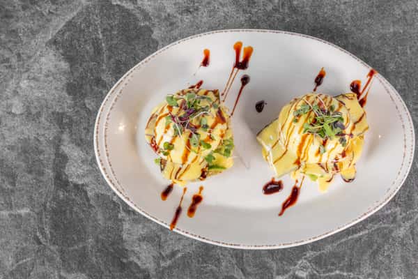 Two servings of avocado toast topped with fresh vegetables, herbs, and creamy sauce, presented on a white plate with decorative drizzles.