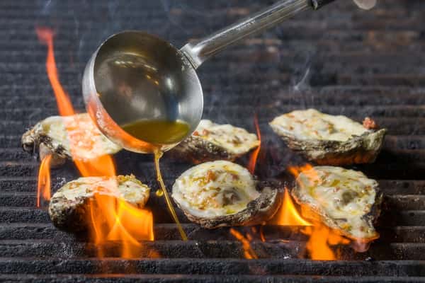 A spoon pouring button over oysters on a flame grill