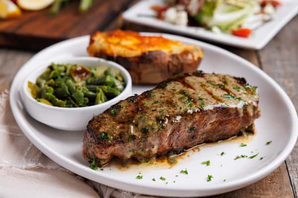 Grilled steak topped with herb butter, served with sautéed green beans and toasted bread, classic steakhouse entrée
