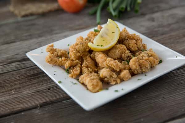 Crispy fried shrimp served with lemon wedge on a white plate, golden seafood appetizer on rustic wooden table