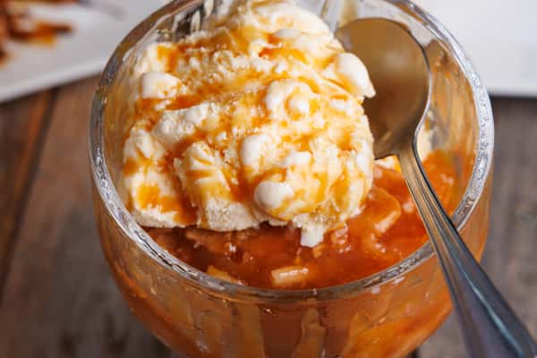 Scoop of vanilla ice cream with caramel drizzle served over warm fruit compote in a glass dish, indulgent dessert close-up