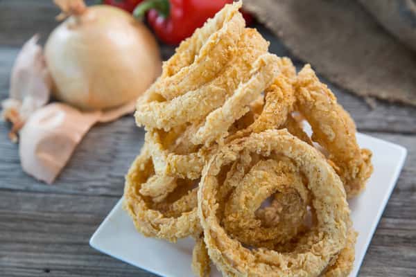 Crispy golden onion rings stacked high on a plate, crunchy fried appetizer with rustic presentation