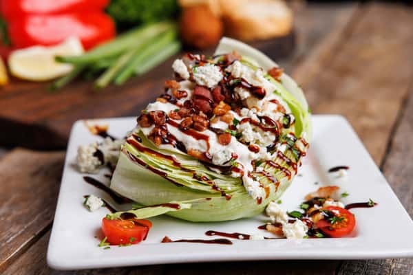 Iceberg wedge salad topped with creamy dressing, crispy bacon bits, crumbled blue cheese, and balsamic glaze, served on a modern restaurant appetizer plate
