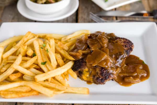 Hamburger steak smothered in brown gravy with sautéed onions, served with golden French fries on a rectangular plate
