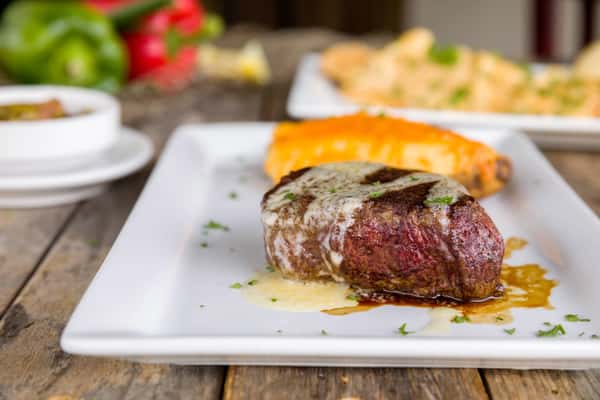 Juicy filet mignon topped with melted butter, served with baked potato and side dishes, upscale steakhouse entrée