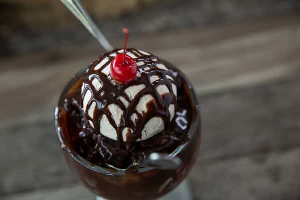 Chocolate sundae with vanilla ice cream, rich chocolate syrup, and a cherry on top in a glass dish, classic dessert