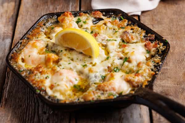Cheesy baked seafood dip with shrimp and herbs, served in a skillet with a lemon wedge, creamy appetizer