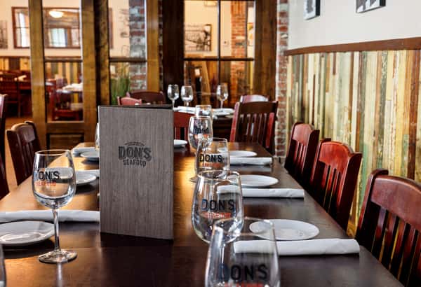 A dining table setup with plates, glasses, wrapped silverware and Don's Seafood menus on display