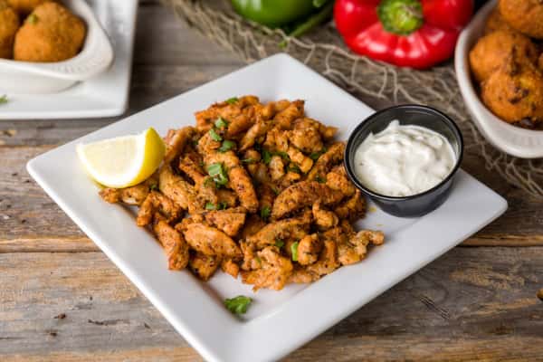Crispy fried calamari seasoned with spices, served with lemon wedge and creamy dipping sauce on a white plate, casual seafood appetizer