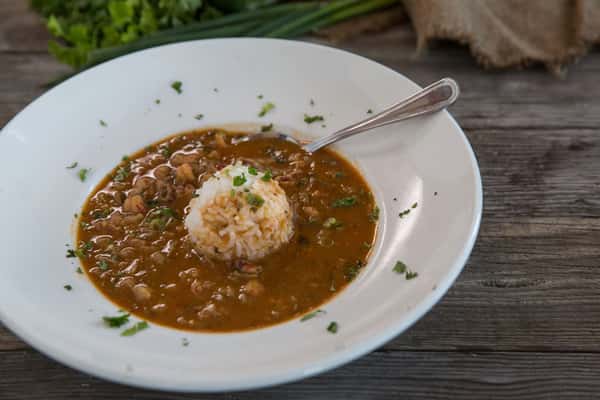 Hearty lentil soup with herbs and a mound of rice in a white bowl, rustic comfort food presentation on wooden table