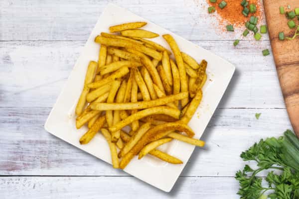 Seasoned French fries on a white plate with a light dusting of spices, simple side dish on a clean background