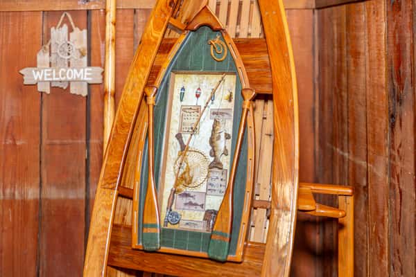 Wooden canoe shelf with fishing-themed decorations including a rod, oars, net, and fish art, beside a rustic "Welcome" sign.