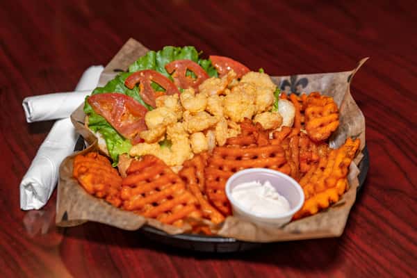 Fried shrimp po'boy sandwich with lettuce and tomato, served with crispy waffle fries and a side of dipping sauce.