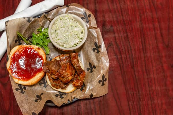 BBQ beef sandwich on a bun with barbecue sauce, served with a side of creamy coleslaw in a small bowl.