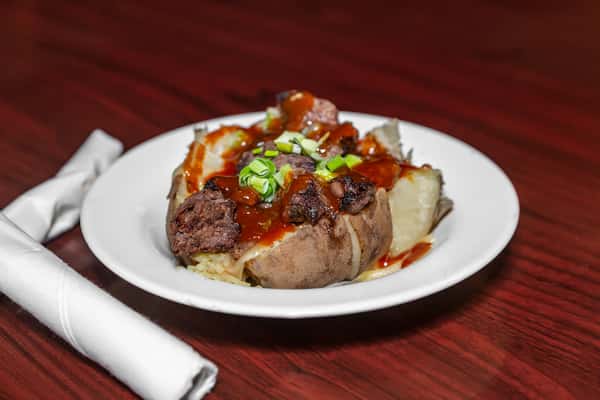 Loaded baked potato topped with grilled steak bites, barbecue sauce, and chopped green onions.