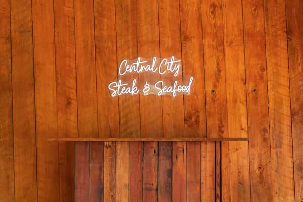 Neon sign reading "Central City Steak & Seafood" mounted on a wooden plank wall with a small ledge below it.