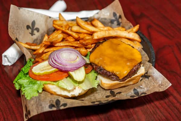 Cheeseburger with lettuce, tomato, pickles, and onions served open-faced with a side of seasoned French fries.