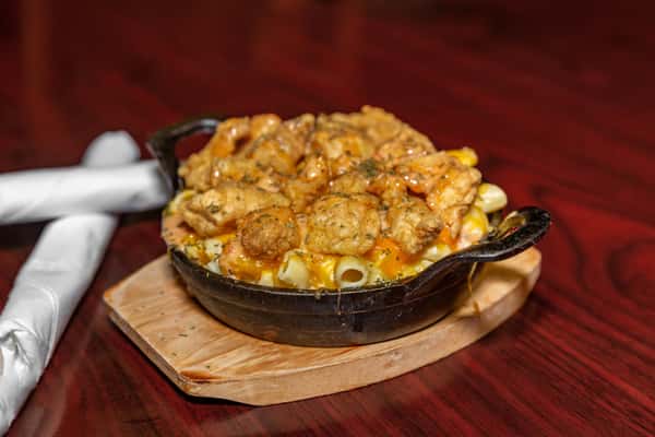 Skillet of creamy macaroni and cheese topped with crispy fried seafood and drizzled with sauce on a wooden serving board.
